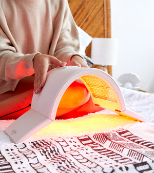 A person using the Elipsa | LightStim, a curved light therapy device emitting a warm glow, placed on a bed covered with a patterned blanket in a cozy bedroom setting.