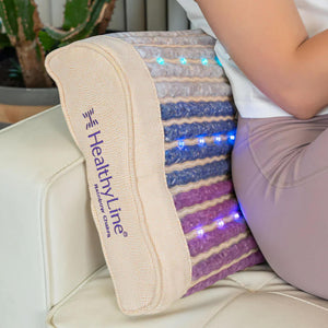 Person sitting on a white couch using the Rainbow Chakra Pillow Soft | HealthyLine, featuring multicolored light therapy panels designed to promote wellness and relaxation.