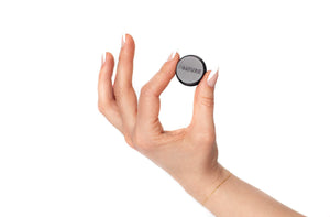Hand holding a small, round wellness device with the label Abature Mini | Abature, showcasing a sleek design suited for skincare and body care routines.