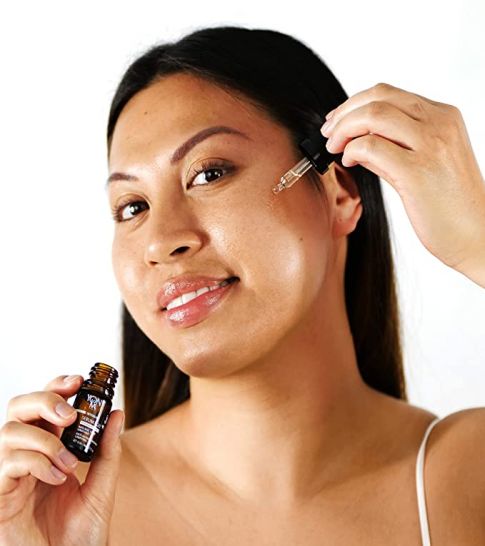 A woman applies Serum C20 | Yon-Ka Paris with a dropper to her cheek, showcasing skincare routine and glowing healthy skin.