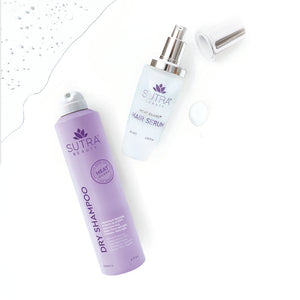 Purple bottle of Heat Guard Dry Shampoo | SUTRA next to a clear bottle of Heat Guard Hair Serum with a silver pump cap on a white surface with water droplets.