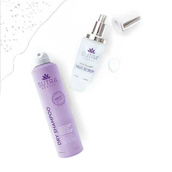 Purple bottle of Heat Guard Dry Shampoo | SUTRA next to a clear bottle of Heat Guard Hair Serum with a silver pump cap on a white surface with water droplets.