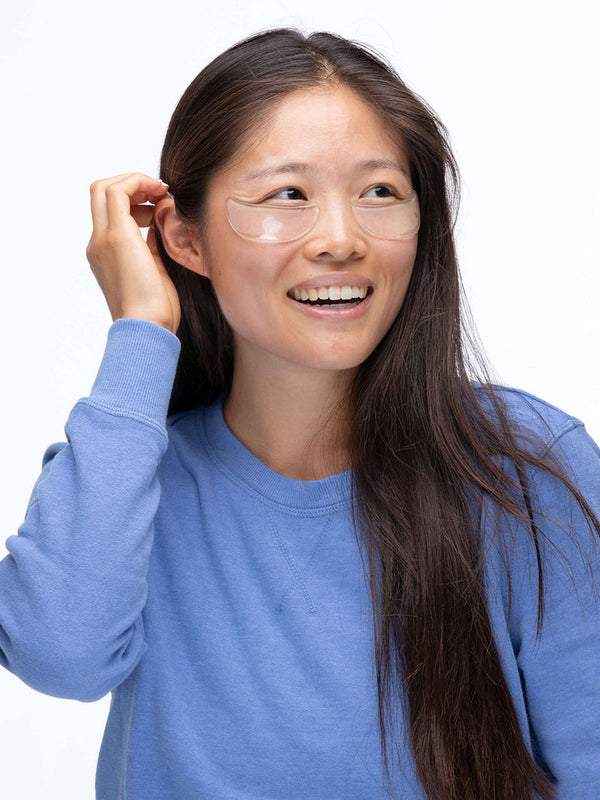 Smiling woman wearing SiliconeFusion™ Eyes & Mouth Patches | Dermaclara under her eyes, demonstrating skincare for reducing wrinkles and promoting hydration.