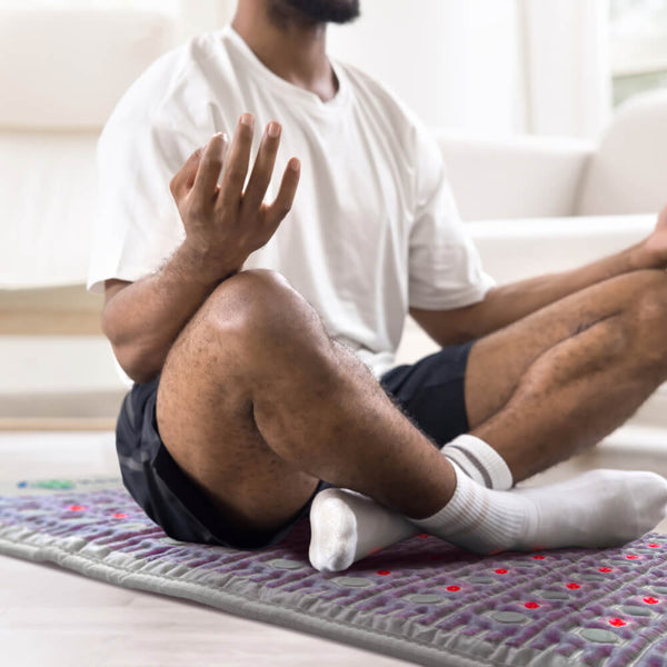 Person meditating in a seated yoga pose on a wellness device mat designed for body care and recovery, featuring the TAJ-Mat™ Full 7224 Firm - Photon PEMF InfraMat Pro® | HealthyLine.