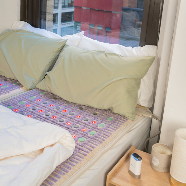 TAJ-Mat™ King 8076 Firm - Photon PEMF Split Inframat Pro® | HealthyLine laid out on a bed with light green pillows and a white comforter by a window in a modern bedroom setting.