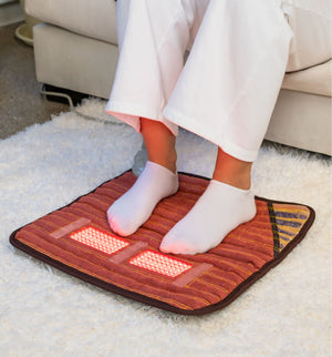 Person sitting on a couch using PEMF Far Infrared Heating Mats | HealthyLine to warm and soothe feet, demonstrating a wellness device for body care and recovery at home.