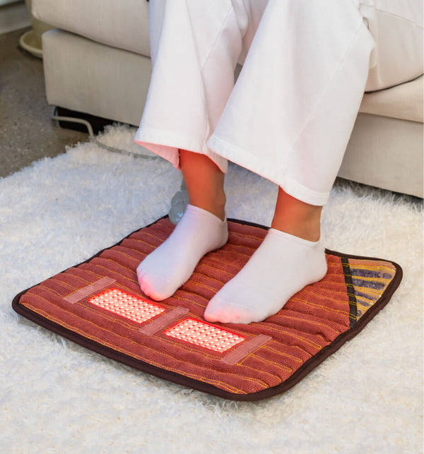 Person sitting on a couch using PEMF Far Infrared Heating Mats | HealthyLine to warm and soothe feet, demonstrating a wellness device for body care and recovery at home.