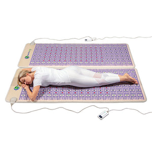 Woman lying on two purple wellness mats with embedded stones, demonstrating use of TAJ-Mat™ Queen 8060 Firm - Photon PEMF Split Inframat Pro® | HealthyLine for body care and recovery.