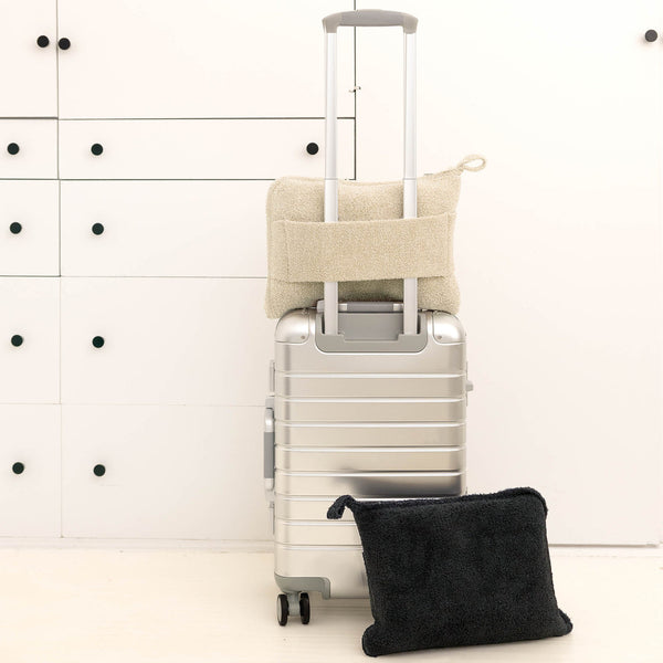 Travel Set (Blanket, Socks, Eyemask, Bag) | Kashwére in neutral tones draped on and next to a silver suitcase, highlighting soft, cozy travel essentials for comfort and wellness.
