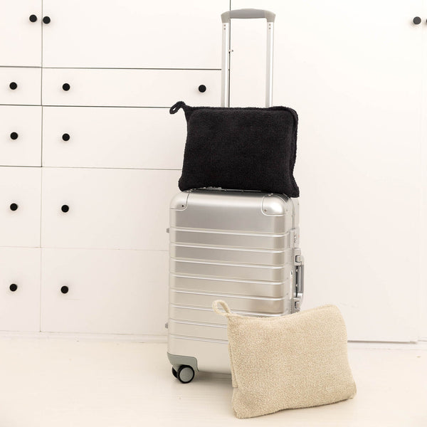 Soft textured travel bag and pouch in neutral tones displayed with silver rolling suitcase, part of the Travel Set (Blanket, Socks, Eyemask, Bag) | Kashwére.