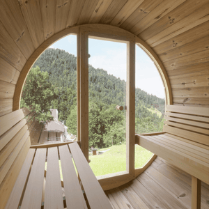 Interior view of the E7G Barrel Sauna - 4-6 Person | Western Sol showing wooden benches and a large circular window door with a scenic mountain and forest view, promoting wellness and relaxation.