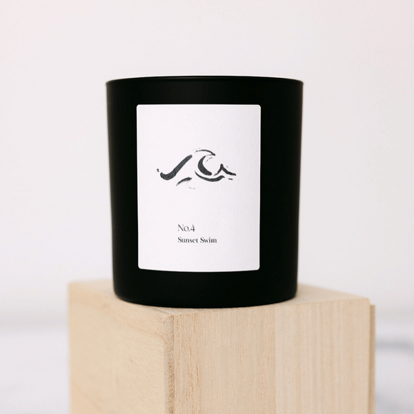 No. 4 Sunset Swim (Amalfi Coast) Candle | Lucky Owl in a minimalist black glass container with white label featuring abstract wave design, placed on a light wooden block.