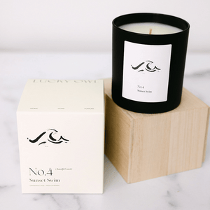 No. 4 Sunset Swim (Amalfi Coast) Candle | Lucky Owl in a matte black glass jar with minimalist white label, displayed next to its cream-colored packaging on a wooden block.