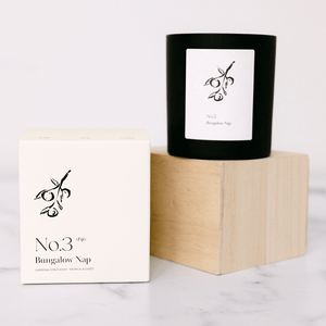 Minimalist black candle and white packaging featuring botanical illustration, displayed on a wooden block with the label No. 3 Bungalow Nap (Fiji) Candle | Lucky Owl.