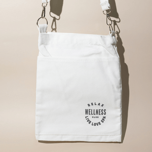 White canvas mini tote bag with adjustable strap featuring black circular text that reads "Relax Wellness Club Live Love Spa," designed for carrying skincare or wellness items, Wellness Club Mini Tote | Live Love Spa.