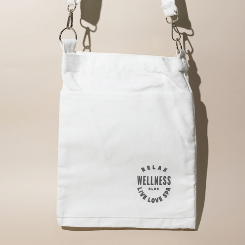 White canvas mini tote bag with adjustable strap featuring black circular text that reads "Relax Wellness Club Live Love Spa," designed for carrying skincare or wellness items, Wellness Club Mini Tote | Live Love Spa.