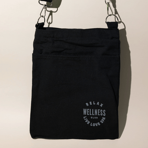 Black fabric mini tote featuring a front pocket and adjustable strap with printed text reading Relax Wellness Club Live Love Spa, designed for easy carrying Wellness Club Mini Tote | Live Love Spa.