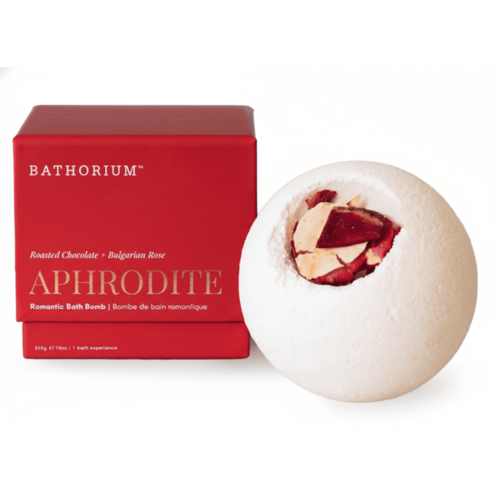 A white round bath bomb with dried rose petals on top displayed next to its red box packaging labeled Aphrodite Bath Bomb | Bathorium, featuring roasted chocolate and Bulgarian rose scents.