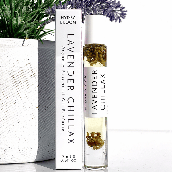 Lavender Chillax Organic Perfume Roll-on | Hydra Bloom featuring clear glass bottle with visible lavender buds and white cap beside white box packaging, placed near green plant.