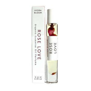 Rose Love Organic Perfume Roll-on | Hydra Bloom with a clear glass bottle containing oil and rose petals, displayed next to its white packaging for skincare and wellness use.