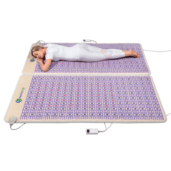 Woman relaxing on a purple wellness device mat designed for body care and recovery, titled TAJ-Mat™ King 8076 Firm - Photon PEMF Split Inframat Pro® | HealthyLine, with controls visible.
