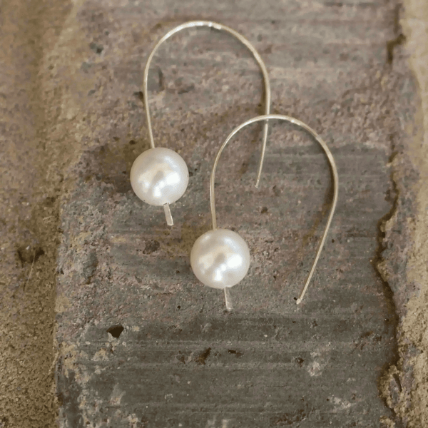 Madeline Pearl Drop Earrings | Liv & B featuring elegant white pearls on delicate silver hooks displayed on a rustic textured surface.