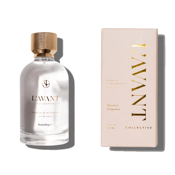 Clear glass bottle with a textured gold cap containing Room Spray | L'AVANT Collective, alongside its matching beige packaging with gold lettering, highlighting Blushed Bergamot scent.