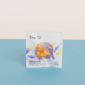 Packaging of Blue Lotus Whole Flower Tea | The Qi featuring a white packet with blue and yellow floral design accents, placed against a blue and light beige background.