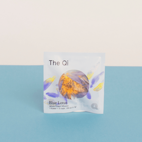 Packaging of Blue Lotus Whole Flower Tea | The Qi featuring a white packet with blue and yellow floral design accents, placed against a blue and light beige background.