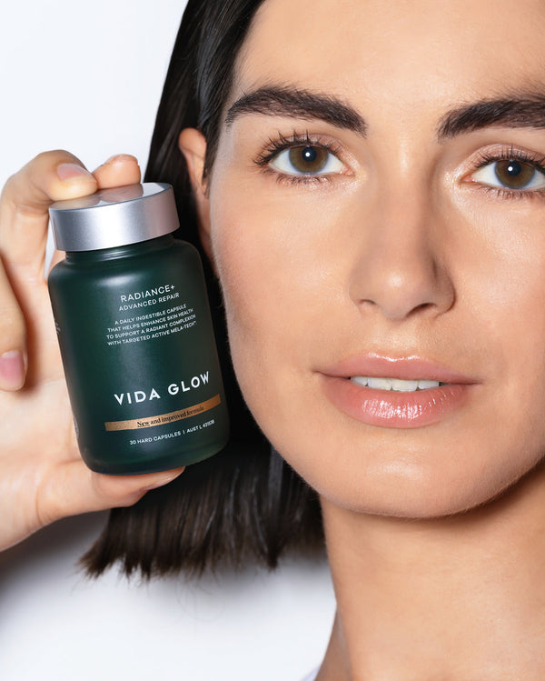 Close-up of a woman holding a dark green bottle of Radiance+ Capsules | VIDA GLOW skincare supplement, highlighting wellness and radiant skin benefits.