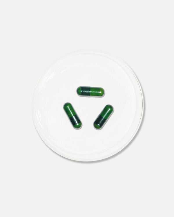 Three green capsules placed on a white dish, representing Radiance+ Capsules | VIDA GLOW wellness supplements for skincare and body care.