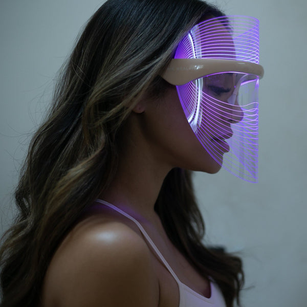 Woman wearing a glowing purple LED Light Therapy Visor | Vie Healing designed for skincare and wellness, shown in profile with wavy brown hair against a neutral background.