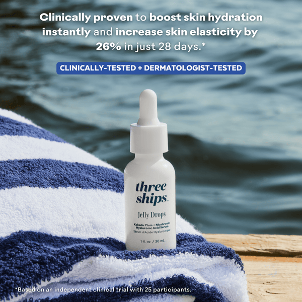 Bottle of Jelly Drops™ Kakadu Plum + Mushroom Hyaluronic Acid Serum | Three Ships placed on a blue and white striped towel by the water, with text highlighting clinical proof of skin hydration boost and elasticity increase in 28 days.