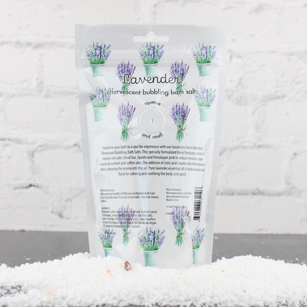 Packaging of Lavender Bubbling Bath Salts | Primal Elements featuring lavender illustrations, set against a white brick background with bath salts scattered in front.
