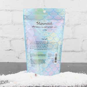 Back view of Mermaid Bubbling Bath Salts | Primal Elements package with iridescent mermaid scale design surrounded by white bath salts on a gray surface.