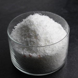 Close-up of a clear glass bowl filled with white granular Mermaid Bubbling Bath Salts | Primal Elements, highlighting the texture for wellness and body care use.