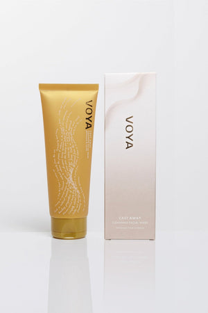 Cast Away Cleansing Facial Wash | VOYA in a gold tube next to its white and beige packaging, both placed on a reflective white surface, showcasing natural skincare.