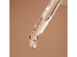 Close-up of a clear dropper releasing a droplet of serum against a soft beige background, highlighting Hyaluronic Self Tanning Serum | NUDA for skincare and body care.