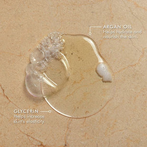 Clear gel drops on a surface labeled to show argan oil that helps hydrate and nourish the skin, and glycerin that helps increase skin’s elasticity, showcasing ingredients for Shower Gel | Moroccanoil.
