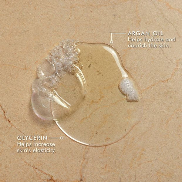 Clear gel drops on a surface labeled to show argan oil that helps hydrate and nourish the skin, and glycerin that helps increase skin’s elasticity, showcasing ingredients for Shower Gel | Moroccanoil.