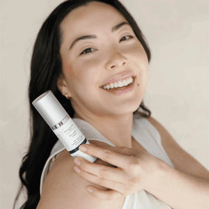 Smiling woman with clear skin holding Bio-Smart Serum | DermaplanePro, showcasing the skincare product in a bright, natural setting promoting wellness.