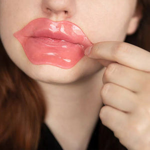 Close-up of a person applying a pink Hydrating Reusable Lip Mask | Dreambox Beauty to moisturize and nourish lips as part of a skincare routine.
