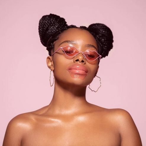 Woman wearing pink tinted sunglasses and a Hydrating Reusable Lip Mask | Dreambox Beauty against a pink background, showcasing skincare and wellness.