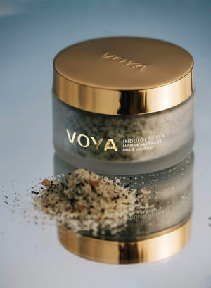 Jar of Indulgent Sea Marine Bath Salts | VOYA with golden lid and reflective surface, showing spilled bath salts blend of natural ingredients including seaweed and citrus elements.