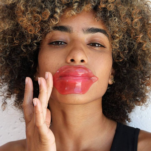 A woman with curly hair applying a pink Hydrating Reusable Lip Mask | Dreambox Beauty for lip hydration and skincare treatment.