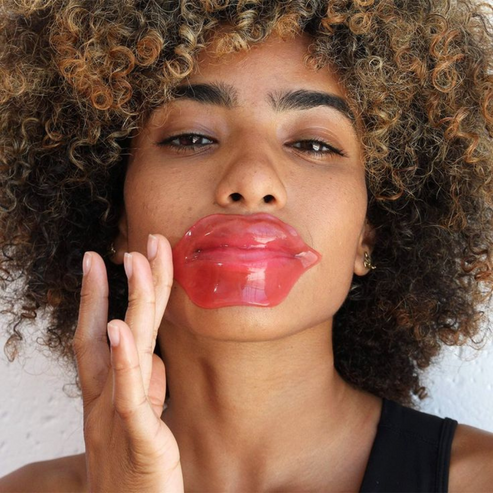A woman with curly hair applying a pink Hydrating Reusable Lip Mask | Dreambox Beauty for lip hydration and skincare treatment.