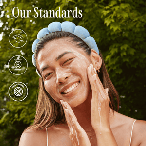 Smiling woman outdoors washing her face with foam, wearing a blue headband, next to text reading "Our Standards" and certification logos, promoting Jelly Drops™ Kakadu Plum + Mushroom Hyaluronic Acid Serum | Three Ships skincare product.