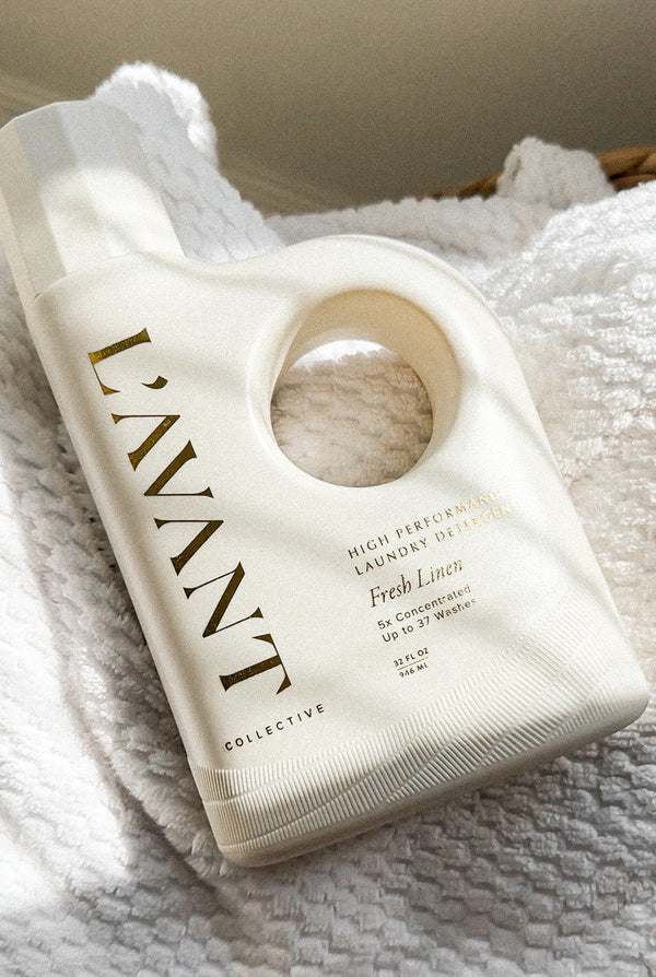 Bottle of High Performing Laundry Detergent - Fresh Linen | L'AVANT Collective resting on soft white textured linens in natural light.