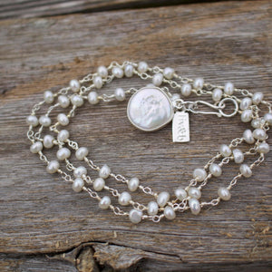 It's A Wrap Triple Pearl Bracelet | Liv & B featuring delicate white pearls on silver chains with a central coin-shaped pearl charm and a silver clasp on a wooden surface.