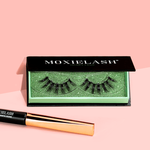 Close-up of Money Lash | Moxielash magnetic eyelashes displayed in a green glitter tray with a black case, alongside a sleek black and rose gold magnetic eyeliner on a soft pink background.